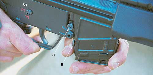 Штатная кнопка (а) базовой НК33 находится с правой стороны винтовки над магазином. Дополнительная кнопка (в), находящаяся перед спусковой скобой, позволяет оперативно отсоединять и присоединять магазин левой рукой, не меняя изготовки и не снимая правую с рукоятки удержания оружия
